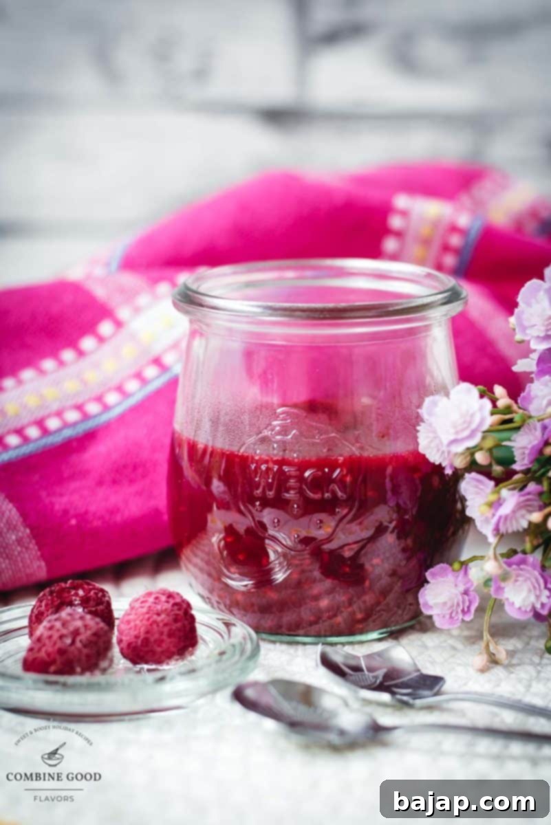 Vibrant raspberry cheesecake topping in a preserving jar, placed on white structured ground.
