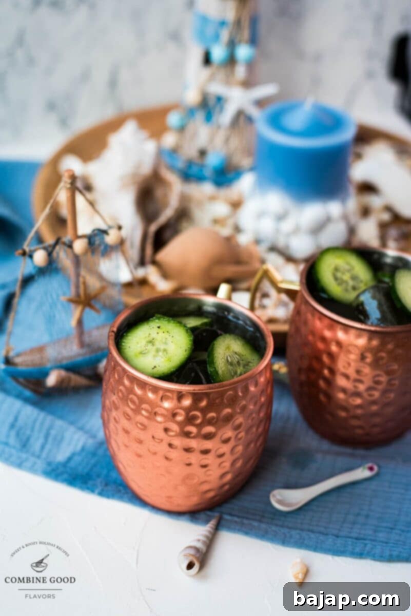 Two refreshing mint cucumber Moscow mules in classic copper mugs, garnished with cucumber slices and mint sprigs, set against a stylish white and blue background, perfect for a summer day.