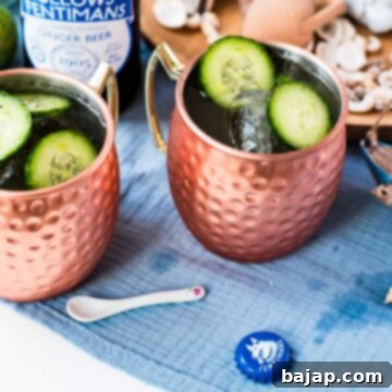 Refreshing mint cucumber Moscow Mule, served in gleaming copper mugs, beautifully presented on a white and blue surface.