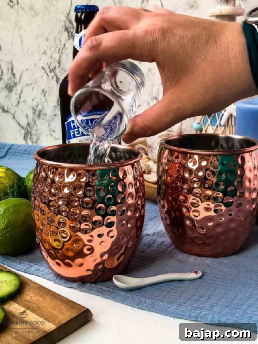Adding unflavored vodka to a copper mug, layering the ingredients after the lime juice for the cocktail base.
