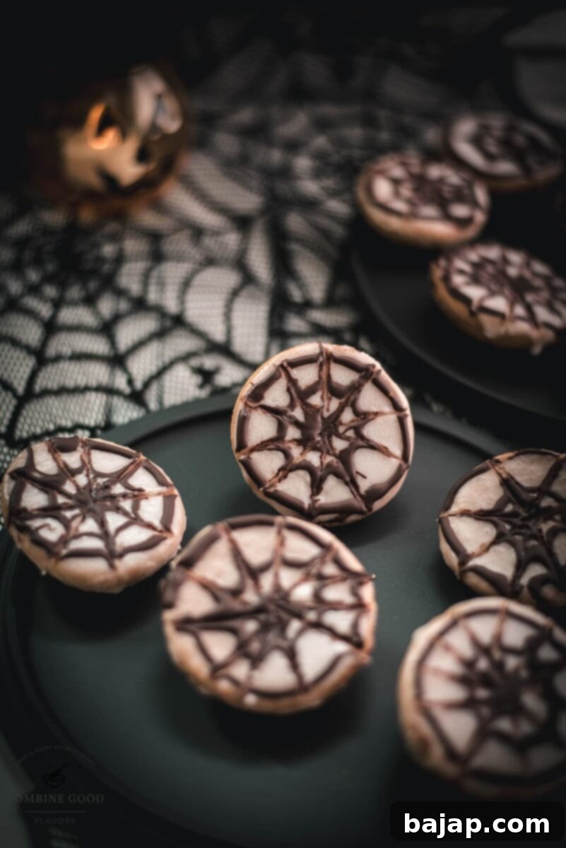 Hauntingly delicious spiderweb cookies, placed on black plate on spiderweb ground. Perfect Halloween party dessert with vanilla custard and dark chocolate.