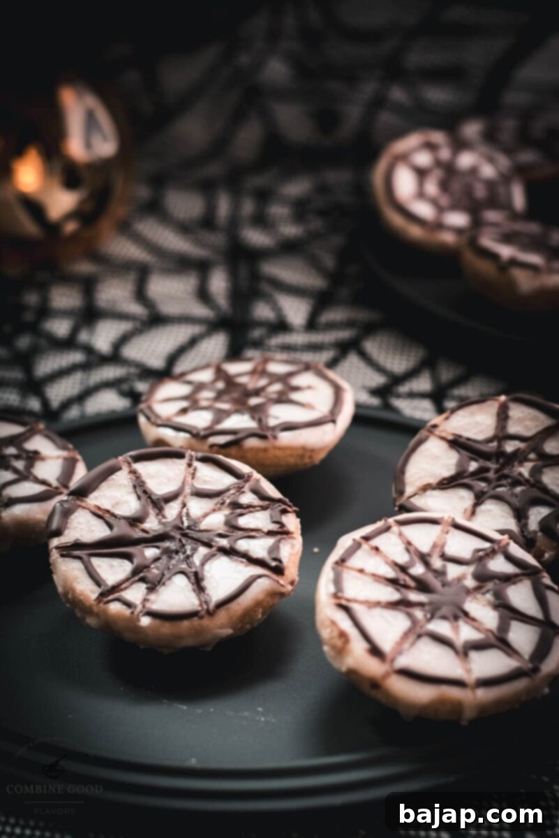 Hauntingly delicious spiderweb cookies, placed on black plate on spiderweb ground. A perfect Halloween dessert.