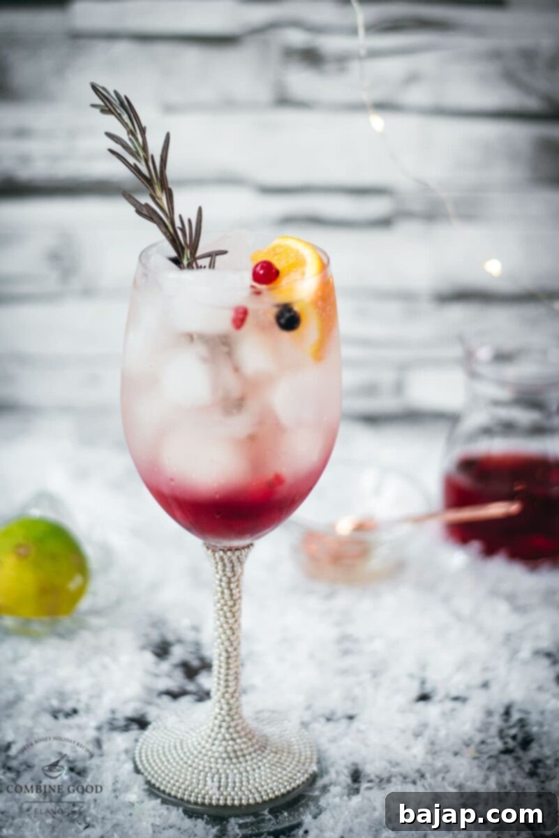 Gorgeous wineglass filled with delicious layered Prosecco Cosmo, garnished with a rosemary twig, an orange slice, and red and black currants, ready to be enjoyed.