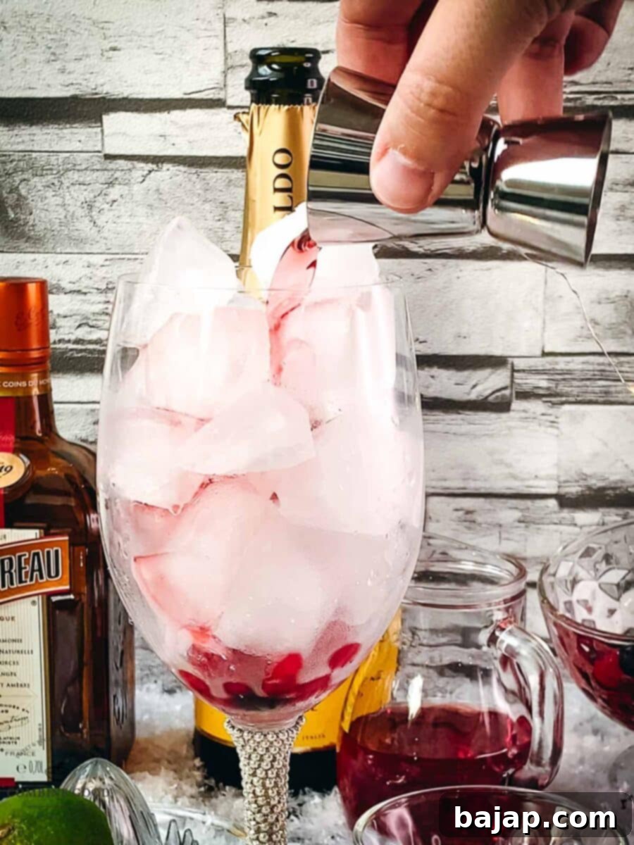 Adding cranberry juice to the wine glass using a jigger, forming the first liquid layer.