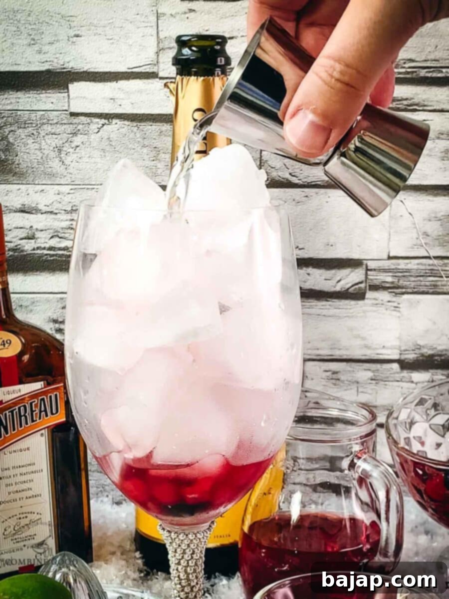 Adding Cointreau to the wine glass using a jigger, layering it with the cranberry juice.