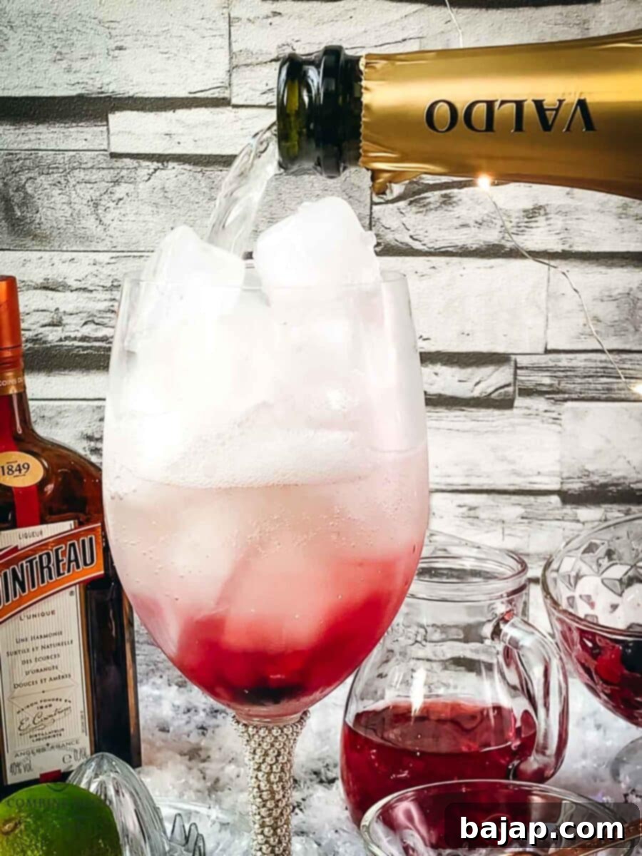 Topping the wine glass with Prosecco, creating the final bubbly layer of the Prosecco Cosmo.