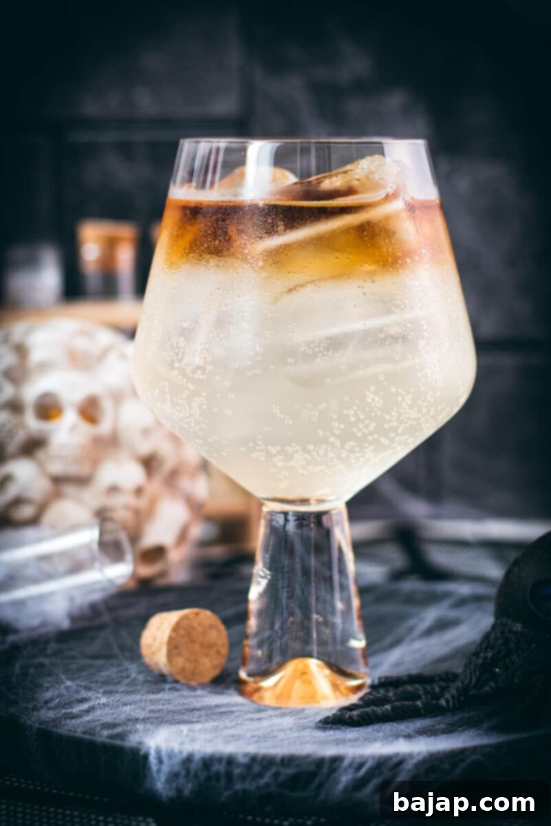 Gorgeous layered kraken ginger beer cocktail with spooky decoration. A dark rum layer sits atop a lighter ginger beer base in a clear glass, adorned with Halloween-themed decor.