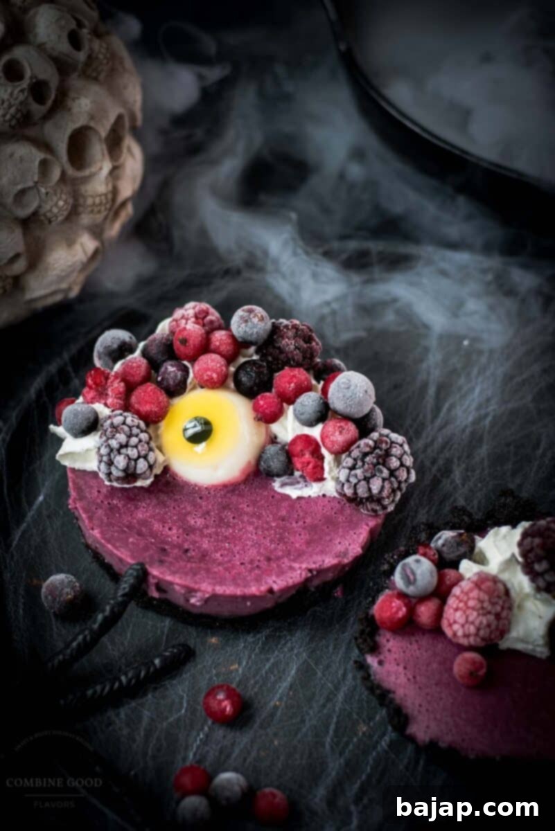 Hauntingly delicious mini Oreo tarts filled with a berry mix ganache, garnished with a creepy gummy eye, frozen berries and whipped cream. Placed on a black plate covered with spider webs.