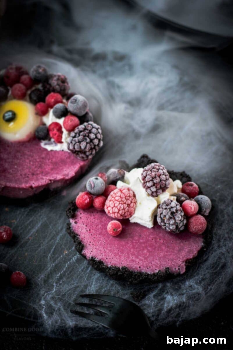 Hauntingly delicious mini Oreo tarts filled with a berry mix ganache, garnished with a creepy gummy eye, frozen berries and whipped cream. Placed on a black plate covered with spider webs.