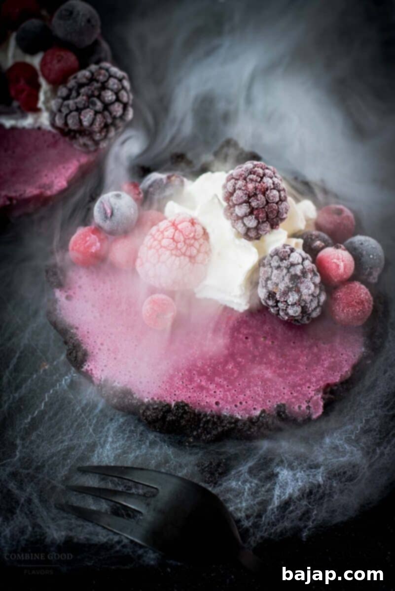 Hauntingly delicious mini Oreo tarts filled with a berry mix ganache, garnished with a creepy gummy eye, frozen berries and whipped cream. Placed on a black plate covered with spider webs.