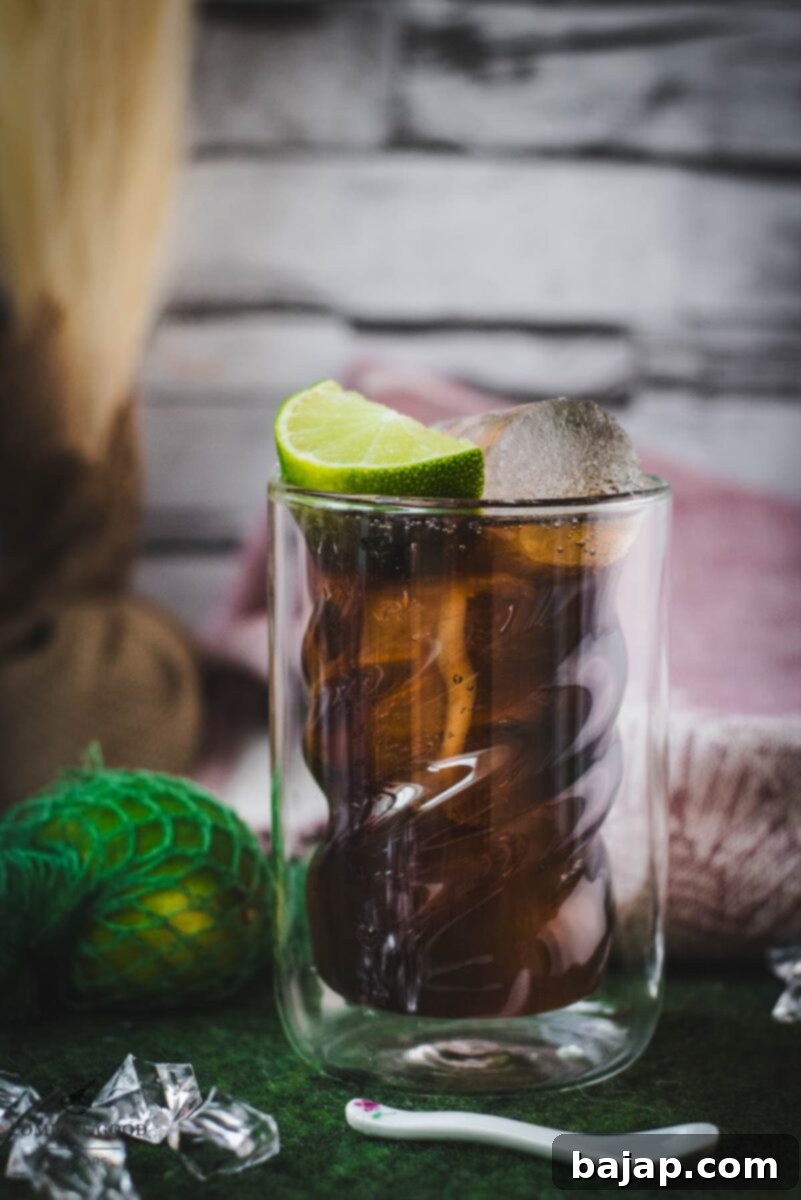 Twisted glass filled with a delicious Cuba Libre cocktail, placed on green felt mat, garnished with a lime wedge.