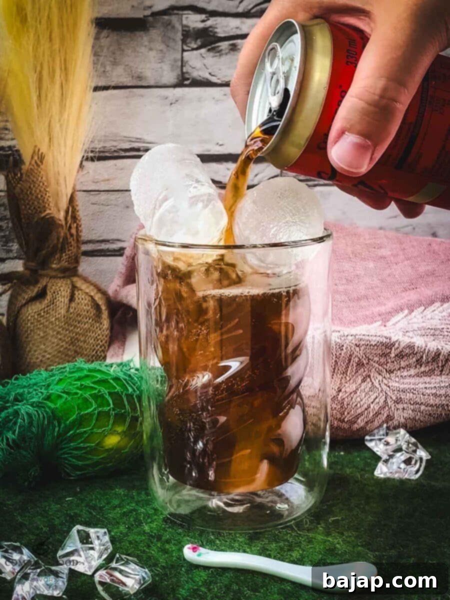 Topping the rum and lime mixture with cola in a highball glass.