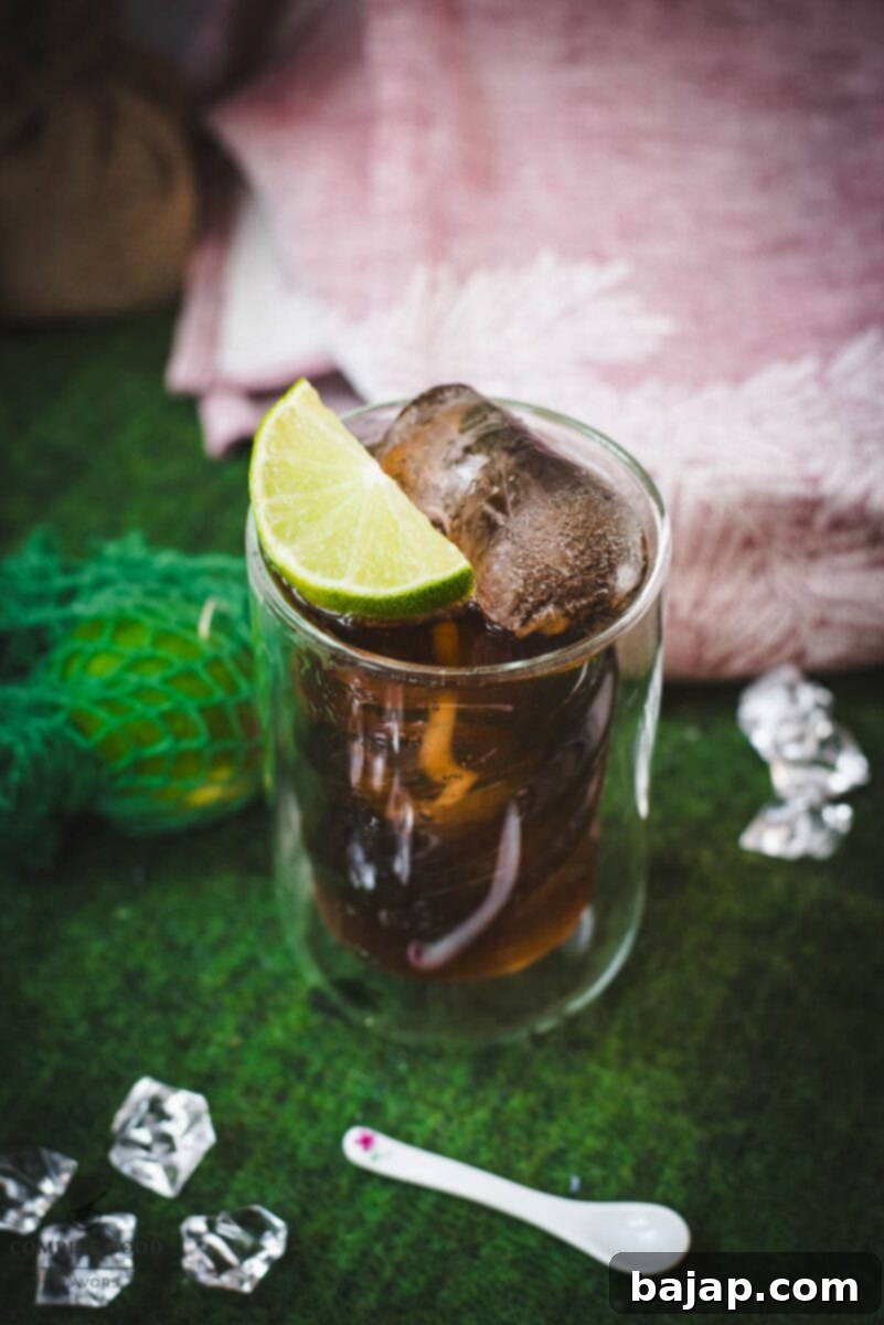 Twisted glass filled with a delicious Cuba Libre cocktail, placed on green felt mat, with condensation on the glass.