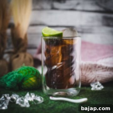 Twisted glass filled with a delicious Cuba Libre cocktail, placed on green felt mat, garnished with a lime wedge.