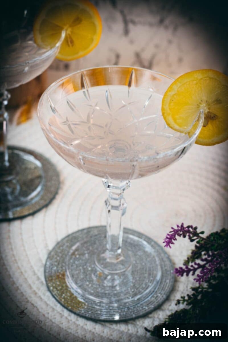 An elegantly presented lavender gin spritz cocktail with prosecco, garnished with a lemon slice and a sprig of lavender, resting on a mirrored coaster.