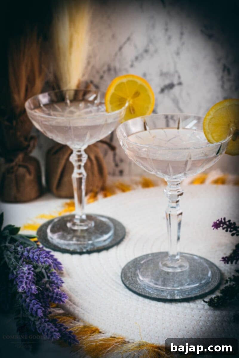 A close-up of an elegant lavender gin spritz cocktail with Prosecco, garnished with a lemon slice, placed on a mirrored coaster.
