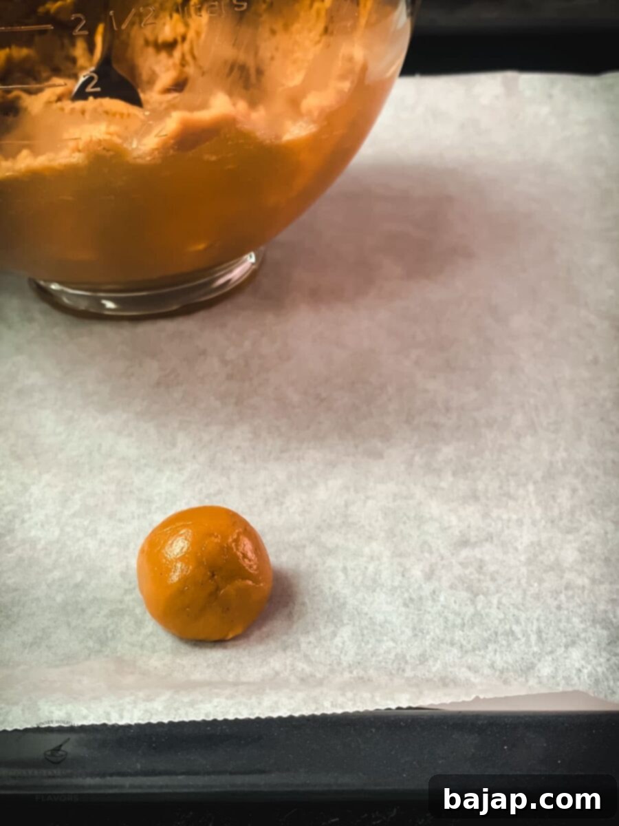 Perfectly rolled peanut butter cookie dough ball placed on parchment paper.