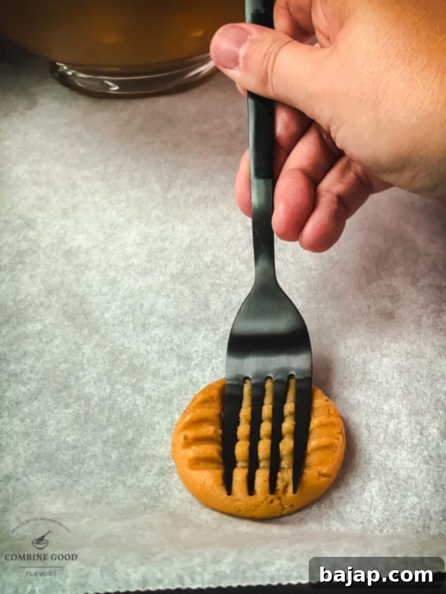 Close-up of a peanut butter cookie with a distinctive fork crisscross pattern on a baking sheet.
