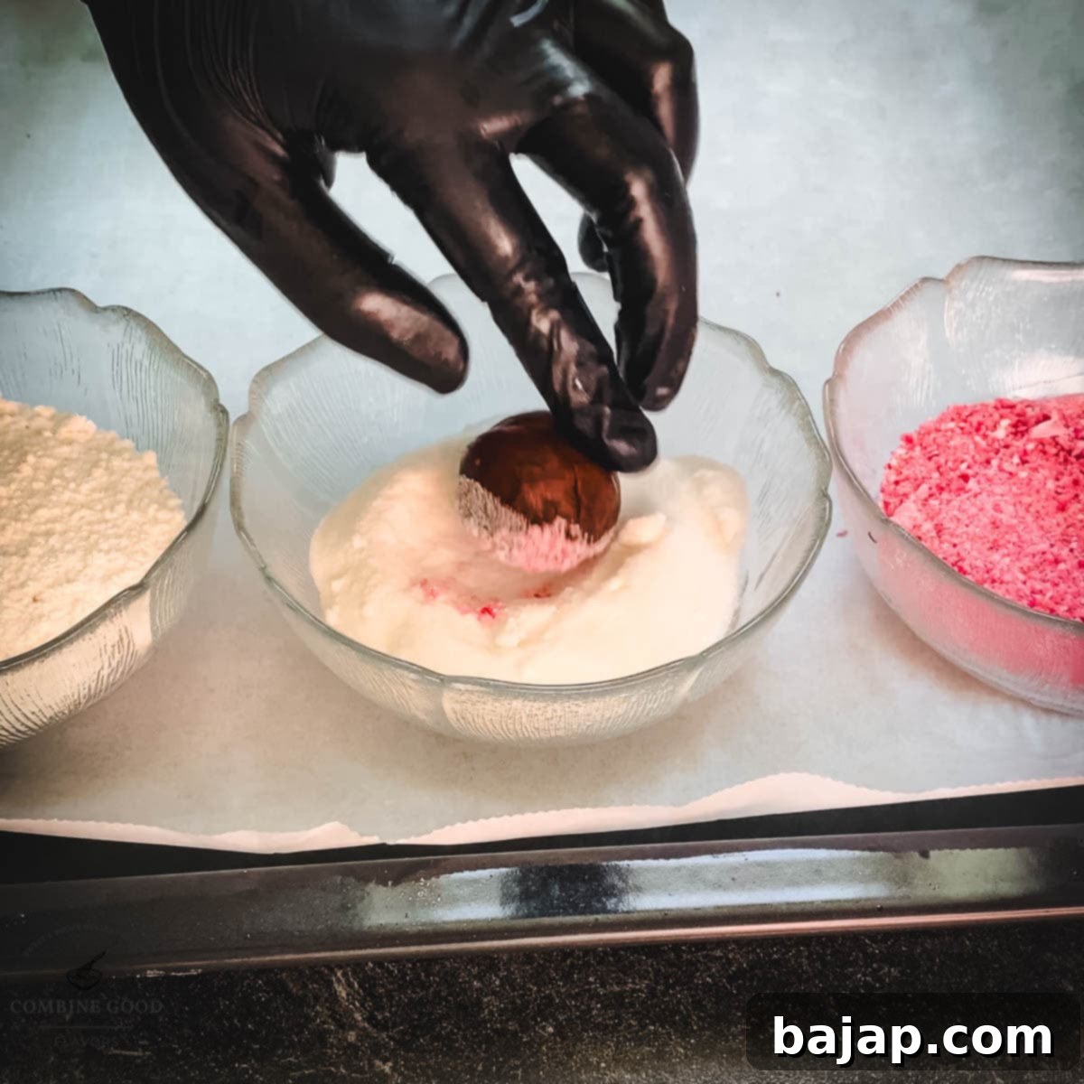 Hand with black gloves holding dough ball over a bowl filled with granulated sugar.