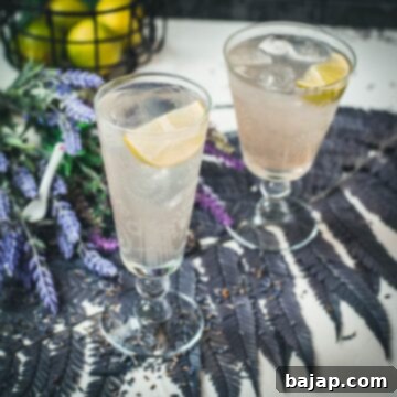 Two beautiful glasses with flower engraving filled with lavender Moscow Mule, arranged on dark blue purple leaves.