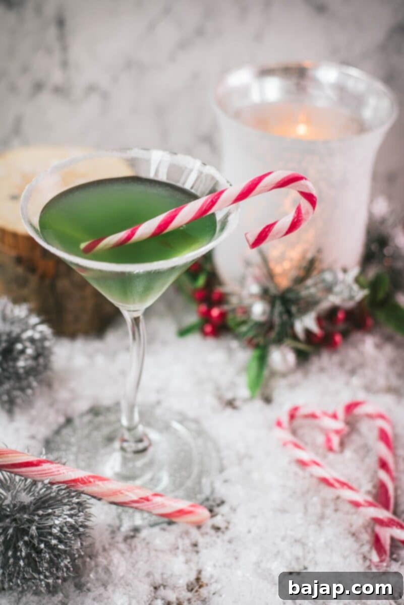 Festive cranberry peppermint martini in sugar rimmed martini glass. Garnished with a candy cane, placed on snowy ground.