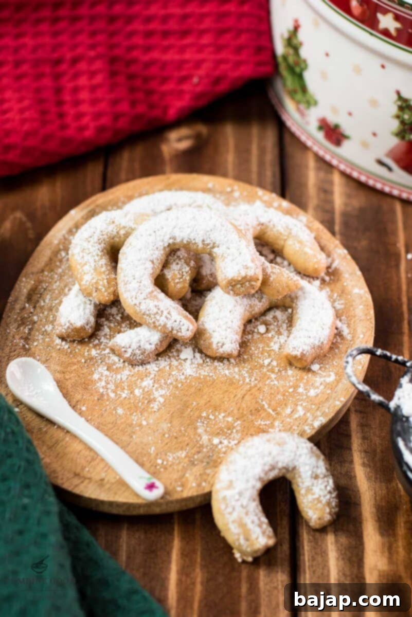 Viennese Vanilla Crescents 11 Delicious traditional Austrian vanilla crescents stacked on wooden plate, placed next to a Christmass cookie jar.