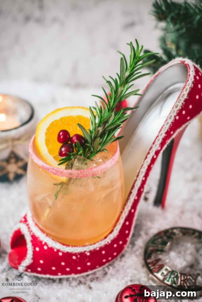 Festive vodka cranberry spritzer, garnished with rosemary twig, orange slice, and cranberries, served in a glass that is placed in a christmassy red high heel.