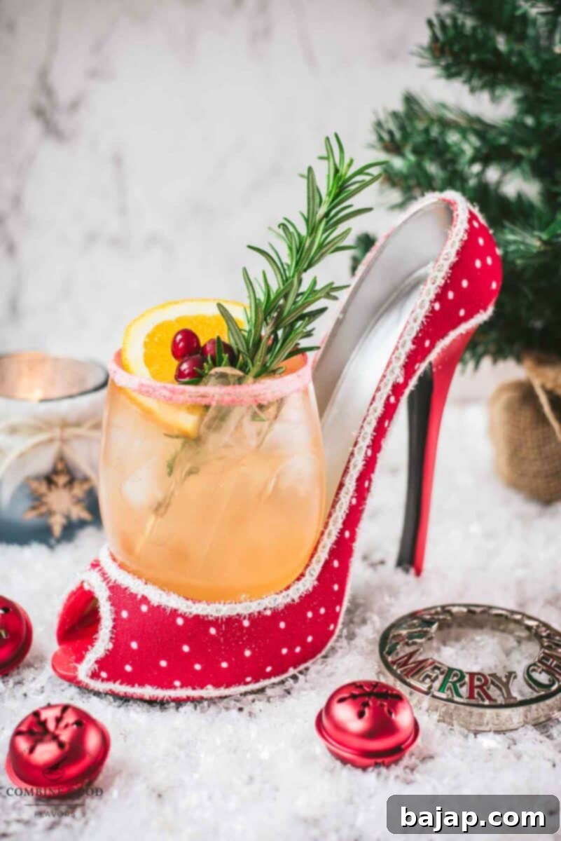 Festive vodka cranberry spritzer, garnished with rosemary twig, orange slice, and cranberries, served in a glass that is placed in a christmassy red high heel, showcasing its holiday charm.