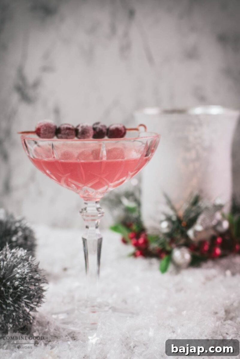 Gorgeous pink cranberry maraschino sour garnished with iced cranberries on a cocktail skewer.