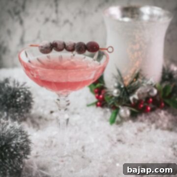 Gorgeous pink cranberry maraschino sour garnished with iced cranberries on a cocktail skewer.