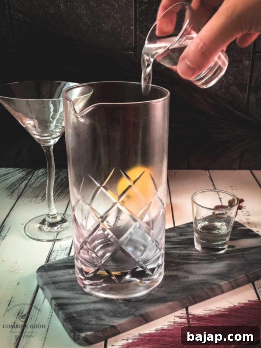 Pouring gin into a chilled stirring glass, a crucial first step for a perfectly balanced classic martini.