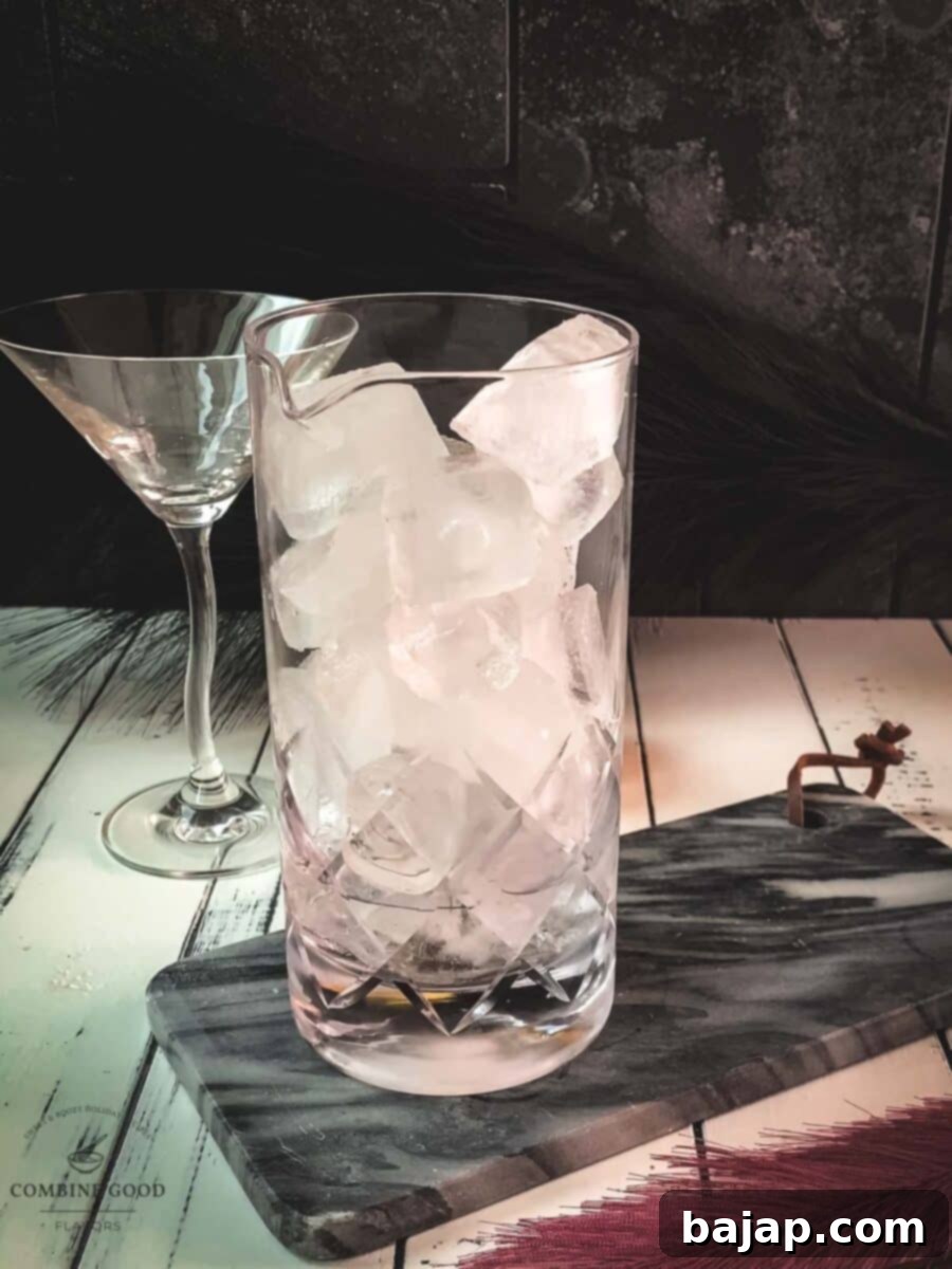 Adding cubed ice to the gin and vermouth mixture in a stirring glass, preparing for the perfect chill.