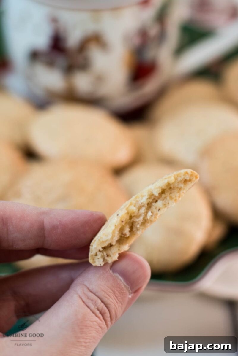 Two fingers holding half a hazelnut meringue cookie in front of a filled cookie plate.