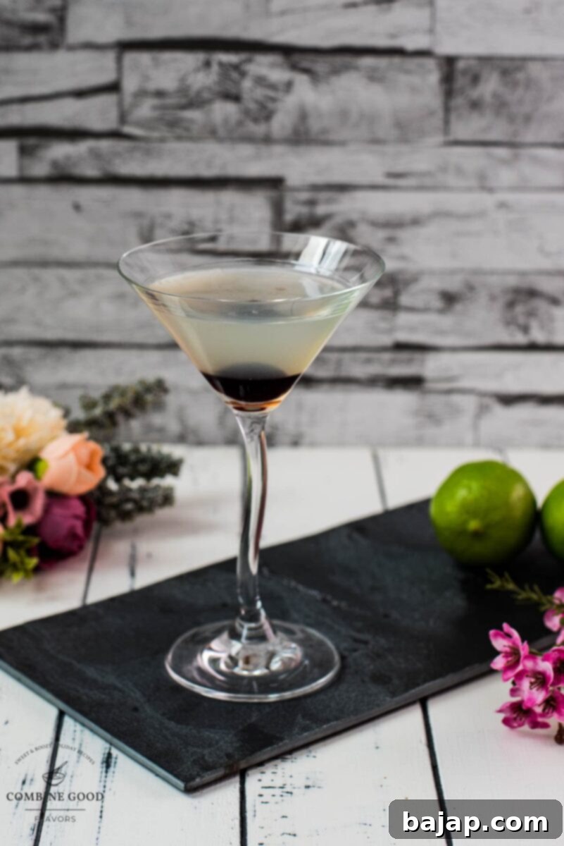 Elegant cocktail glass filled with a delicious aviation cocktail and garnished with a maraschino cherry. Placed on a black slate plate.