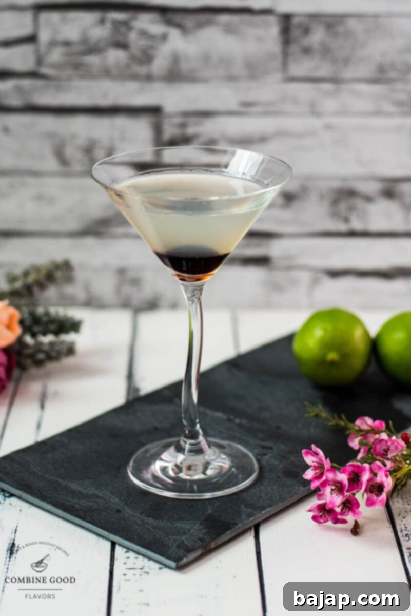 Elegant cocktail glass filled with a delicious aviation cocktail and garnished with a maraschino cherry. Placed on a black slate plate.