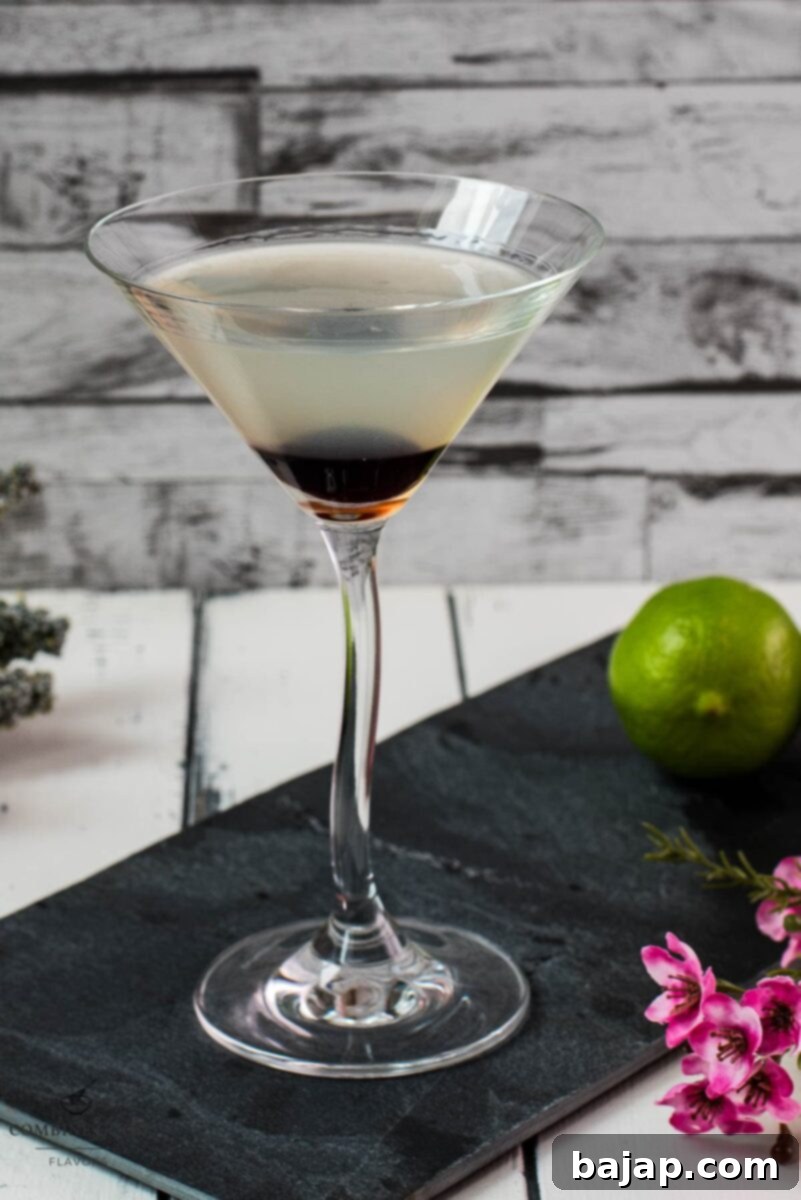 Elegant cocktail glass filled with a delicious aviation cocktail and garnished with a maraschino cherry. Placed on a black slate plate.