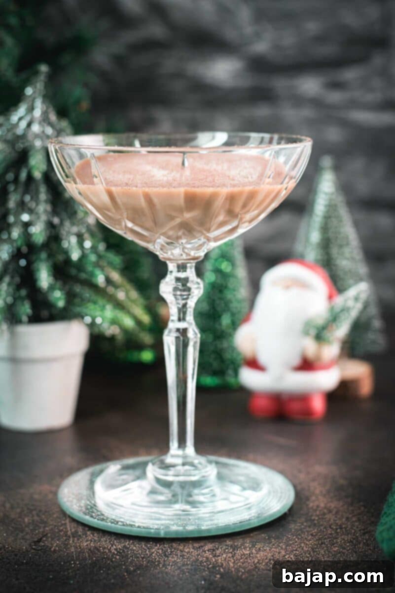 Festive chocolate martini with a white chocolate snowflake garnish, placed on mirrored coaster next to a Santa clause figurine.