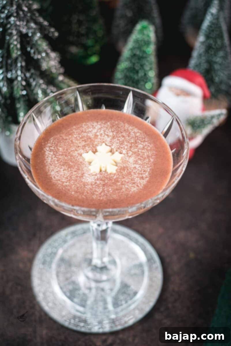 Festive chocolate martini with a white chocolate snowflake garnish, placed on mirrored coaster next to a Santa clause figurine.