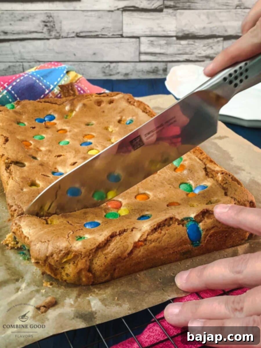 Colorful M and M Cookie Bars 6 A hand cutting a large M&M cookie bar slab into neat squares with a sharp knife.