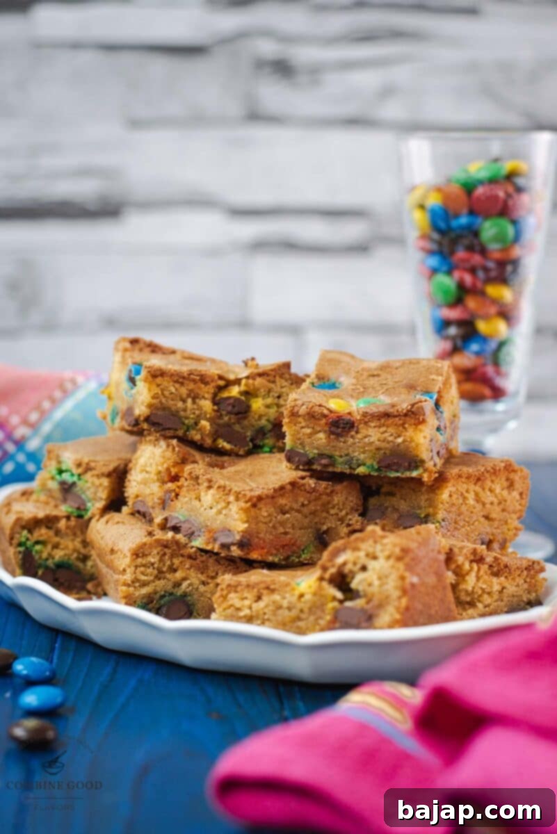 Close-up of a stack of M&M cookie bars on a white plate, highlighting their chewy texture and colorful M&M candies.