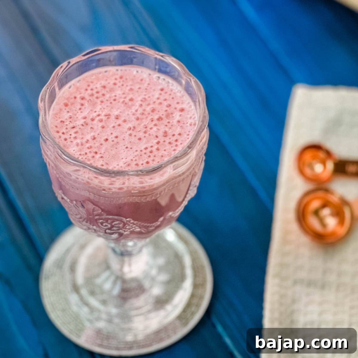 Cute and delicious pink strawberry milk in a gorgeous serving glass. Placed on a glass coaster on blue wooden ground.