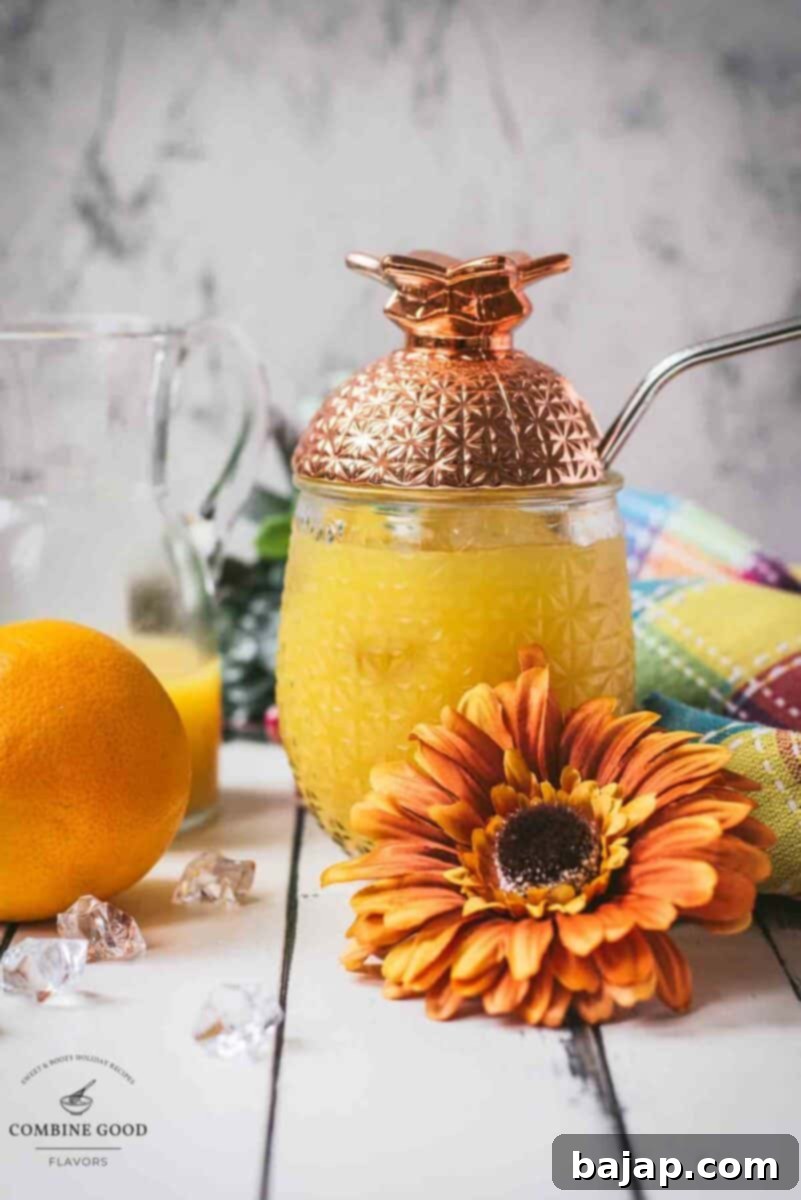 Classic screwdriver cocktail, served in pineapple shaped cocktail glass, placed next to an orange flower.