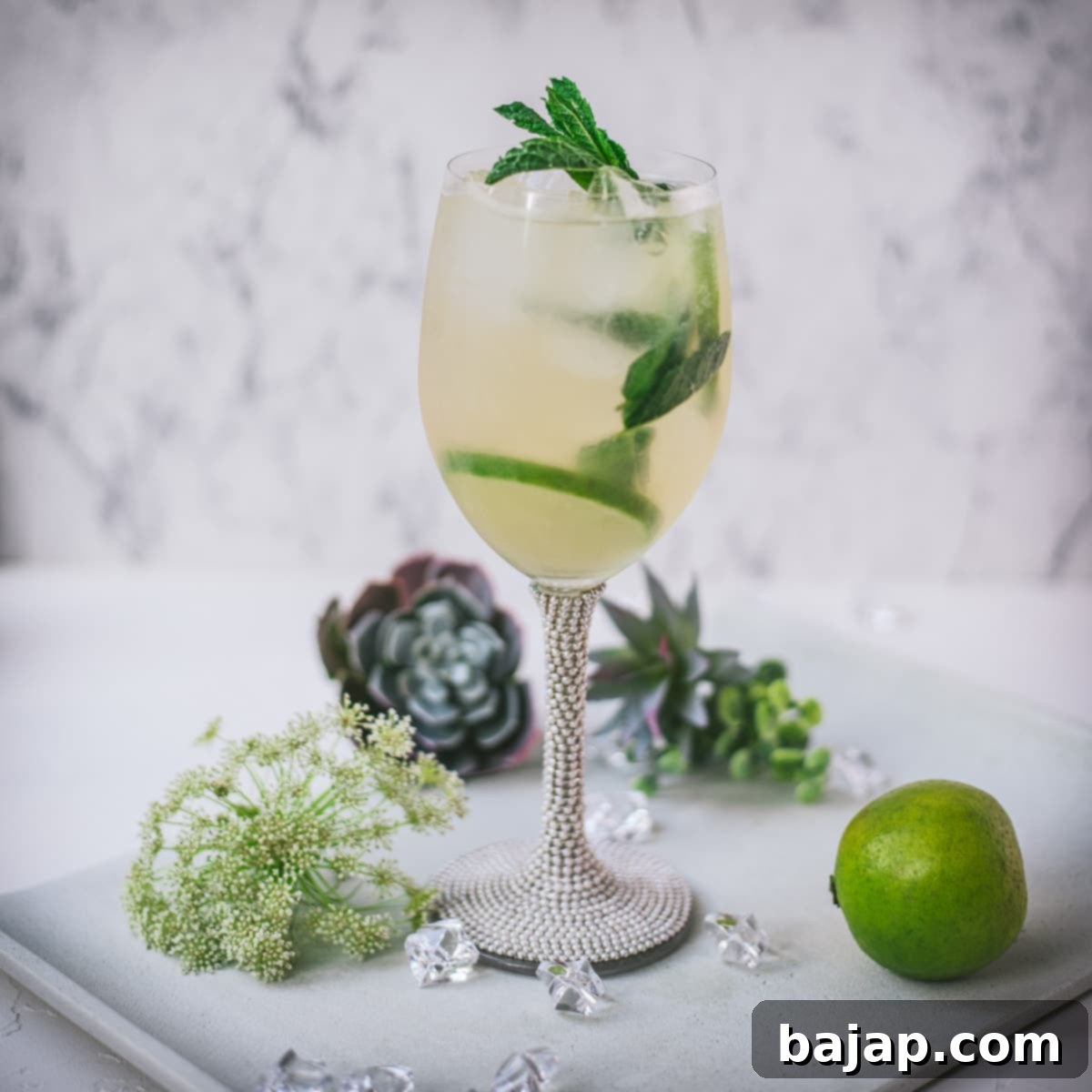 Stunning wine glass filled with Hugo spritz cocktail, placed on a white plate and garnished with mint leaves and lime slices.