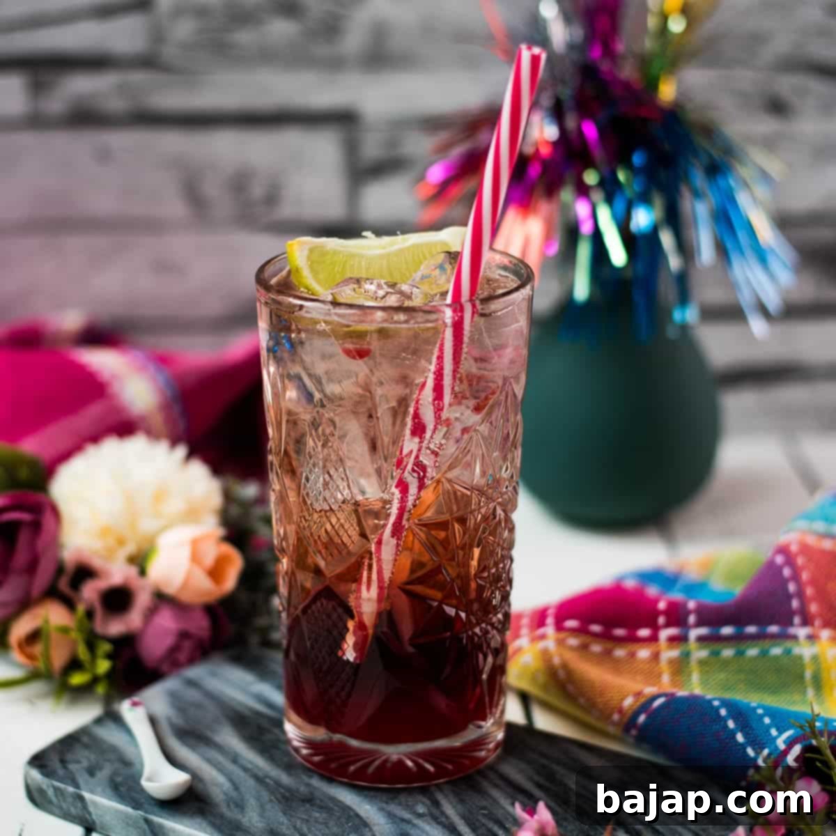 Gorgeous high ball glass filled with raspberry gin tonic, using sloe gin. Garnished with a lime wedge and a drinking straw.