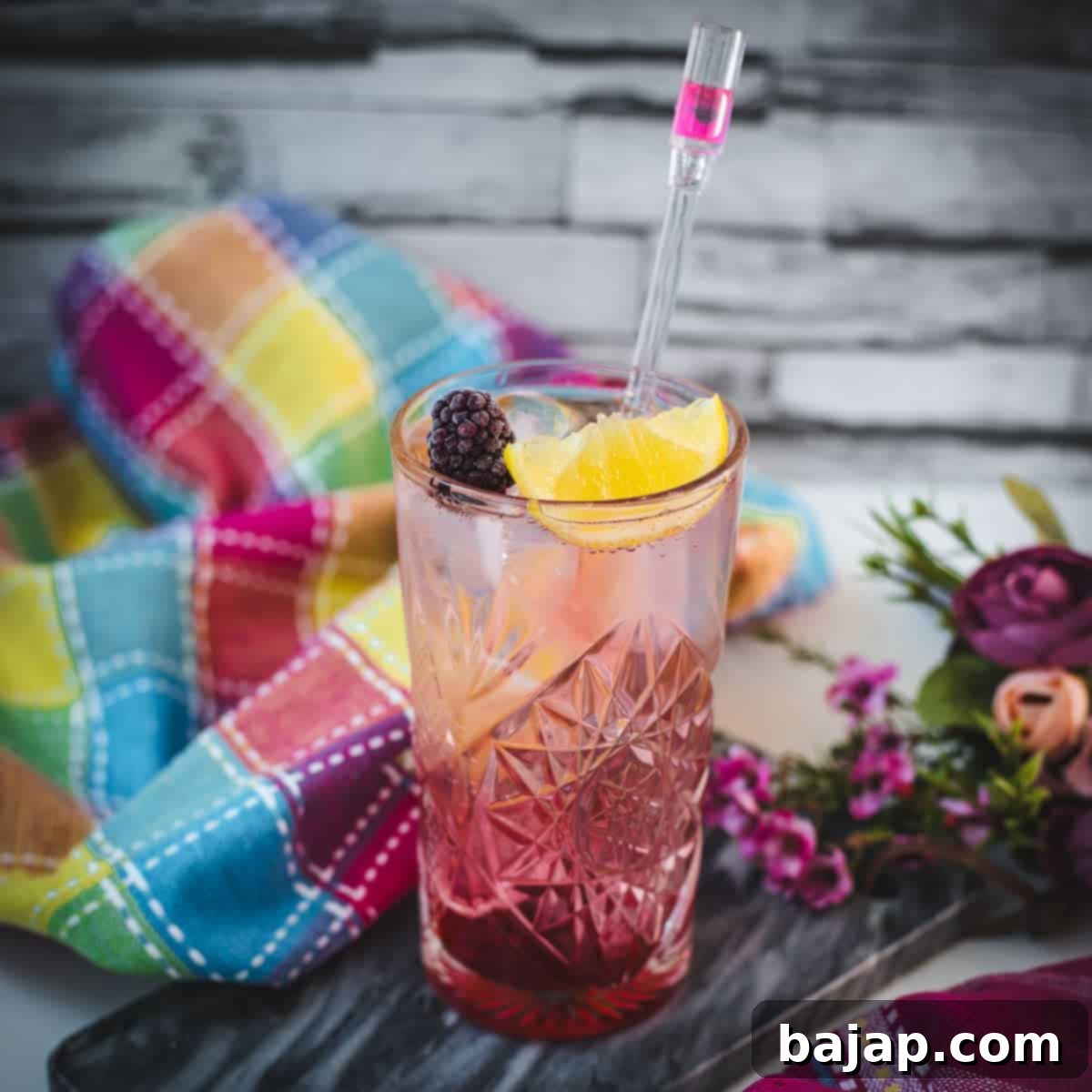 Refreshing blackberry raspberry gin fizz, garnished with a lemon wedge and a blackberry, placed on marbled plate.