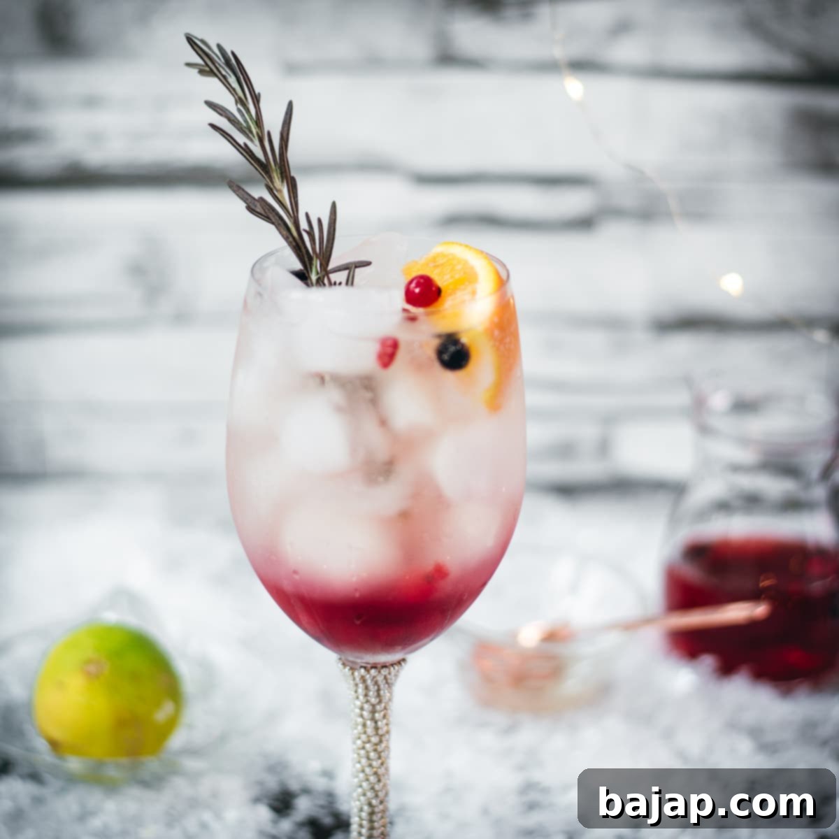 Gorgeous wineglass filled with delicious layered Prosecco cosmo. Garnished with a rosemary twig, an orange slice, and red and black currants.