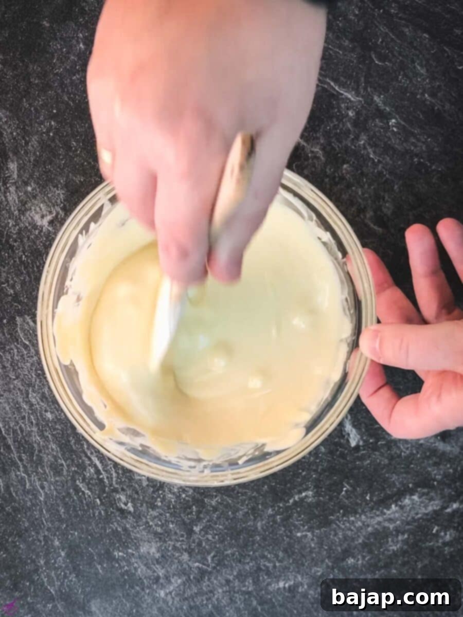 Melted white chocolate ganache being stirred with a spatula until smooth, a crucial step for achieving perfect consistency in the pistachio ganache.