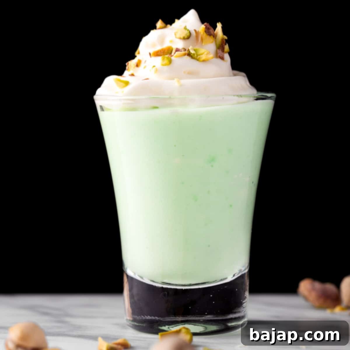 Bright green pistachio pudding shots, garnished with whipped cream.