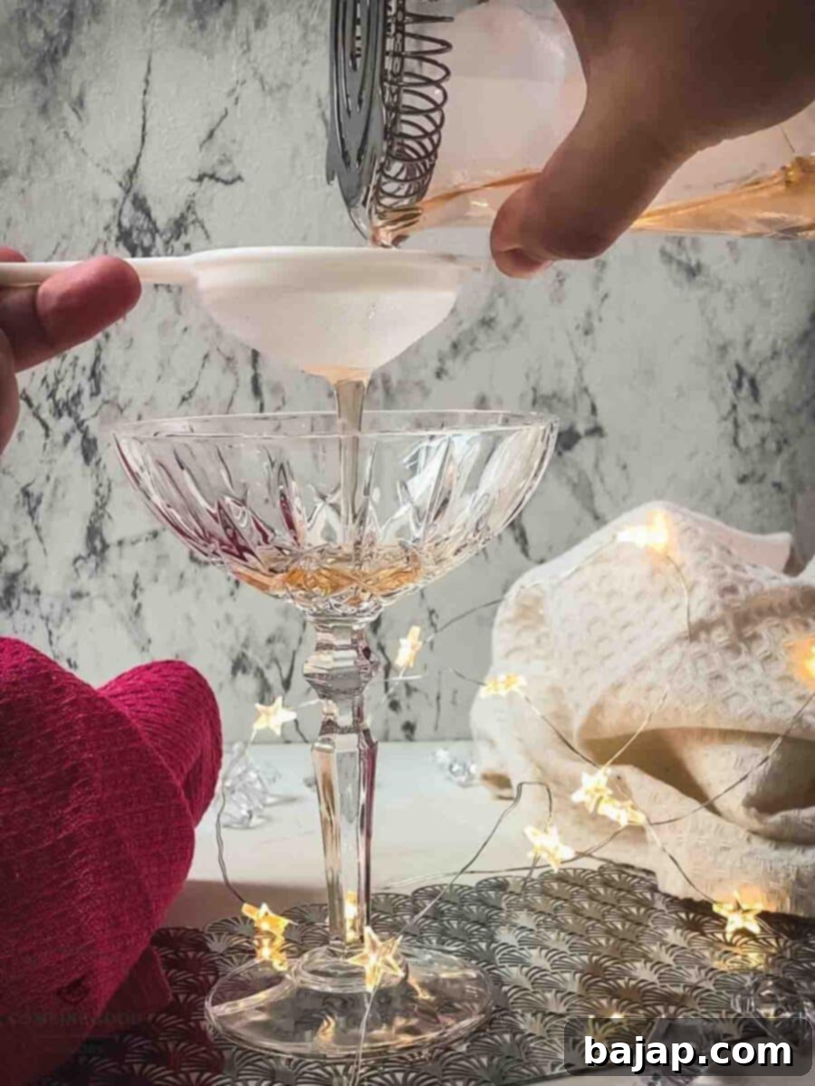 Fine-straining the Pink Gin cocktail into an elegant serving glass.