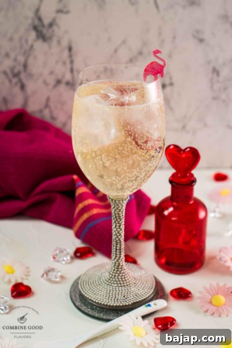 Valentines gin cocktail, garnished with a gorgeous flamingo cocktail pick, served in wine glass. Placed on a mirrored coaster next to a heart shaped flask.